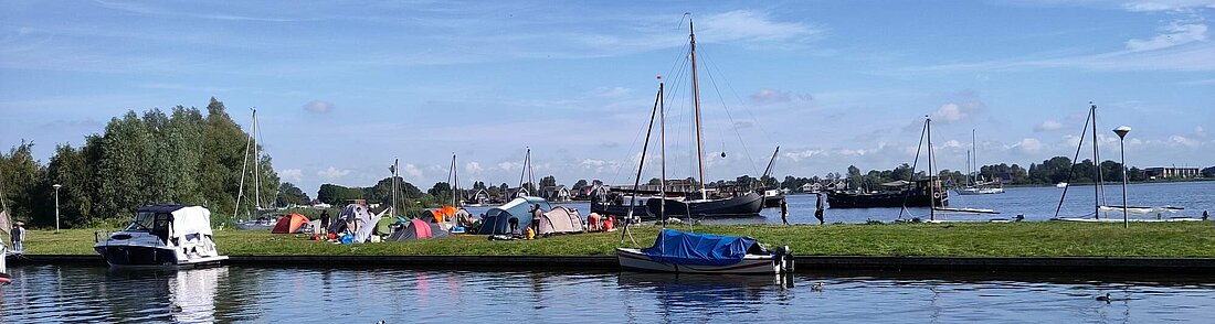 Auf dem Bild zu sehen ist eine Hafeneinfahrt und ein kleines Zeltlager auf einer Wiese