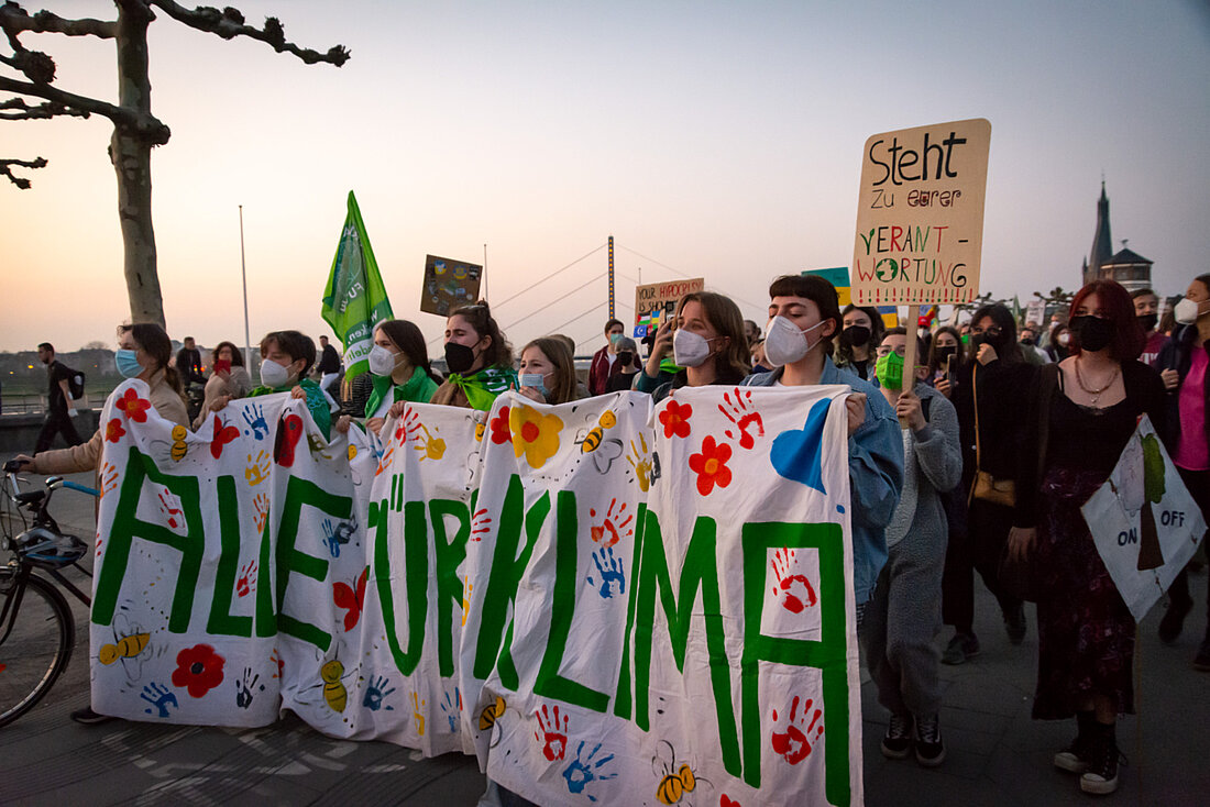 Auf dem Foto sieht man eine Demonstration von den Fridays for Future in Düsseldorf. Im Vordergrund sieht man junge Menschen, die medizinische Masken tragen und ein Banner in der Hand halten auf dem steht „Alle fürs Klima“.