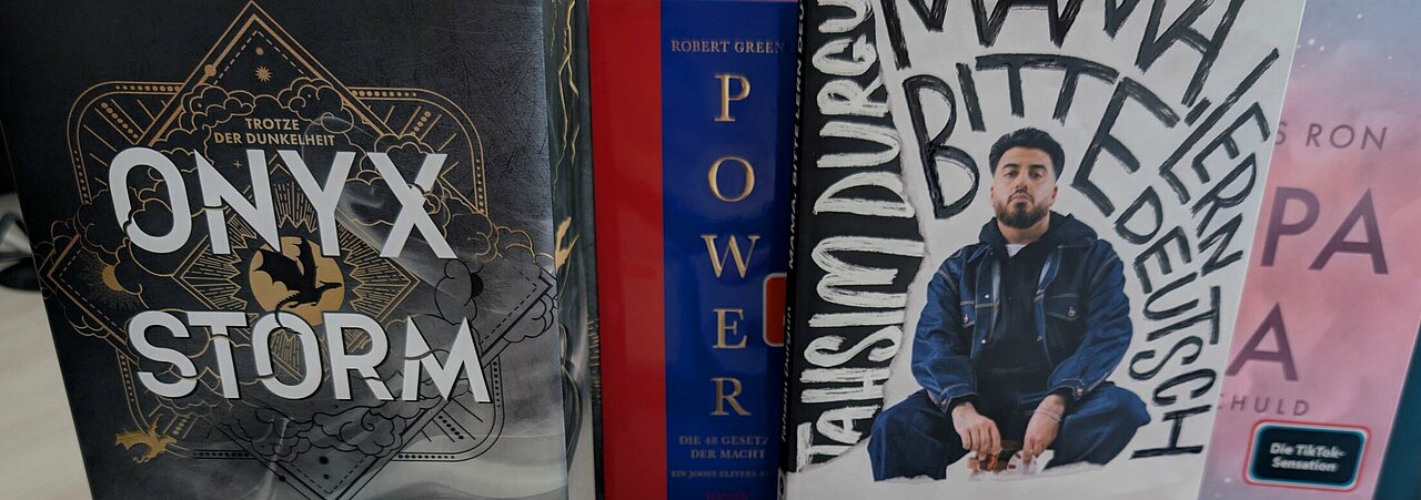 Auf dem Foto sind sechs Bücher zu sehen. Vier stehen nebeneinander, zwei liegen vor den Büchern, die stehen.