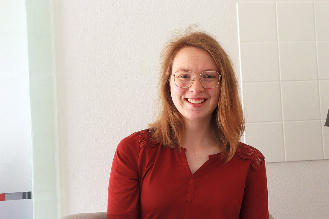 Magdalena fordert die Vergabe von kostenlosen Menstruationsprodukten auch an den Toiletten selbst. Foto: Greta Stangner Magdalena steht vor einer weißen Wand in den Redaktionsräumen des Hochschulradios.