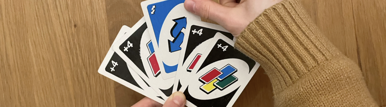 Auf dem Bild sieht man eine Hand, die Uno-Karten hält und eine Richtungswechel-Karte nimmt. 