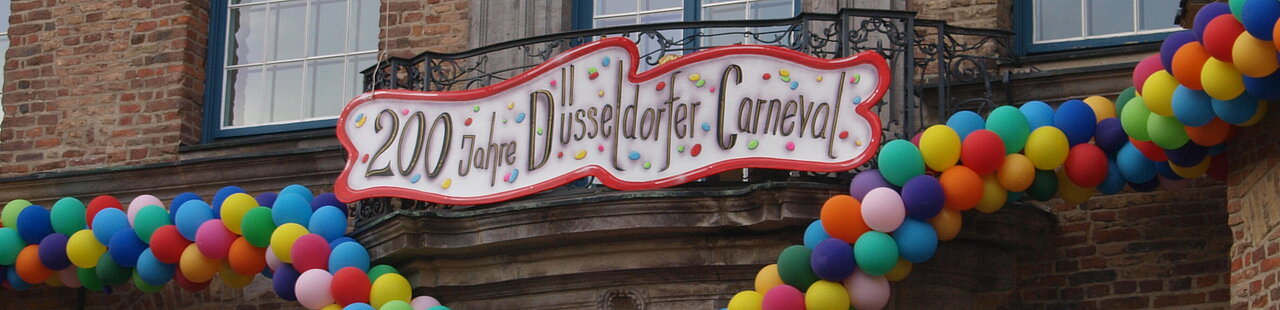 Fassade des Düsseldorfer Rathauses verziert mit bunten Luftballons und einem Schild unter einem Fenster auf dem steht: "200 Jahre Düsseldorfer Carneval"