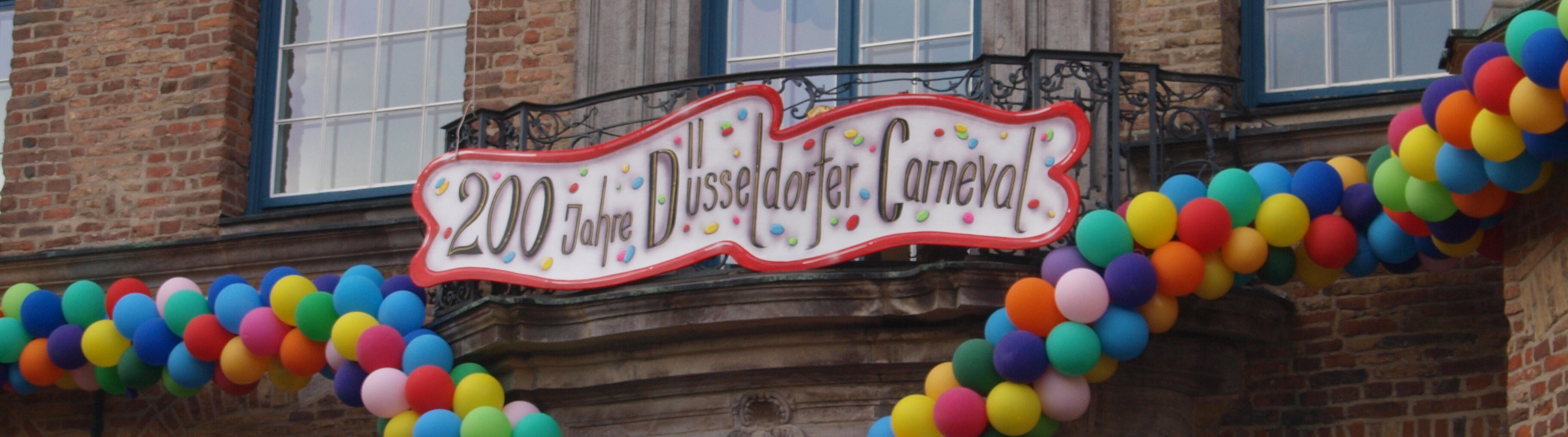Fassade des Düsseldorfer Rathauses verziert mit bunten Luftballons und einem Schild unter einem Fenster auf dem steht: "200 Jahre Düsseldorfer Carneval"