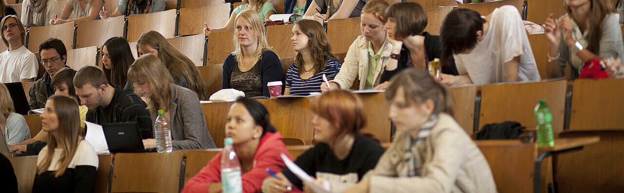 Auf dem Fotos sind Studierende in einem Hoersaal zu sehen. Sie blicken nach vorne.