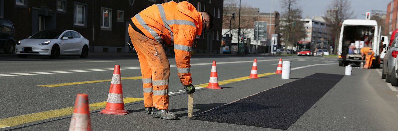 Man sieht Arbeiter, die die Straßenmarkierung der Umweltspur entfernen.