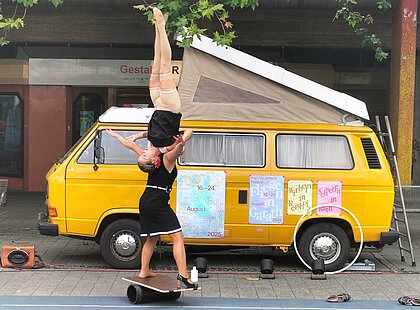 Auf dem Foto sind Lotta und Stina zusehen. Eine Frau steht auf einem Brett, dass auf eine Rolle liegt. DIe andere liegt auf ihren Schultern und streckt ihre Beine kerzengerade in die Luft.