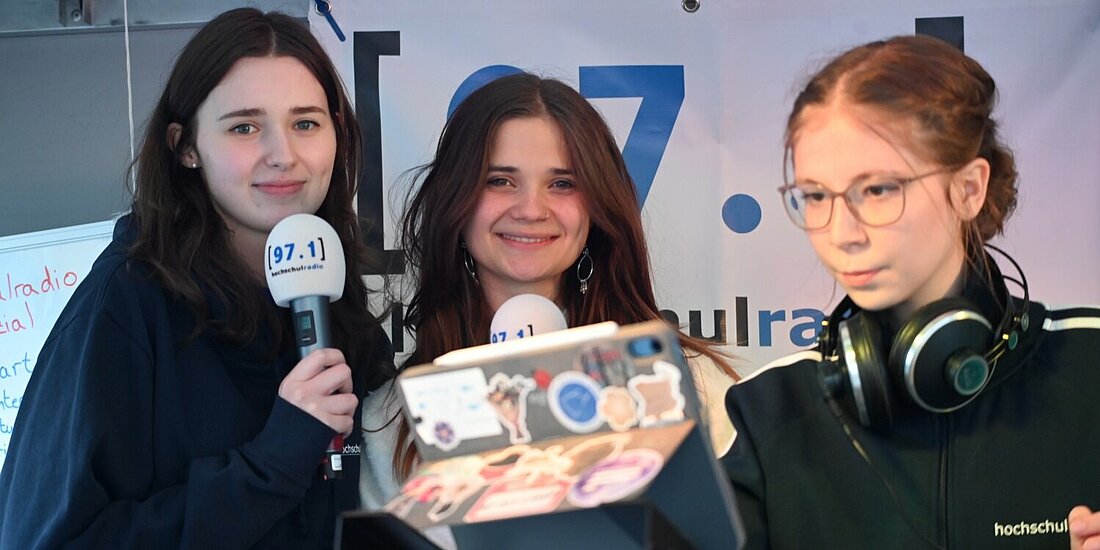 Die cm3-Redakteur:innen Charlotte, Carolin stehen mit Moderatorin Asya auf einer kleinen Bühne.