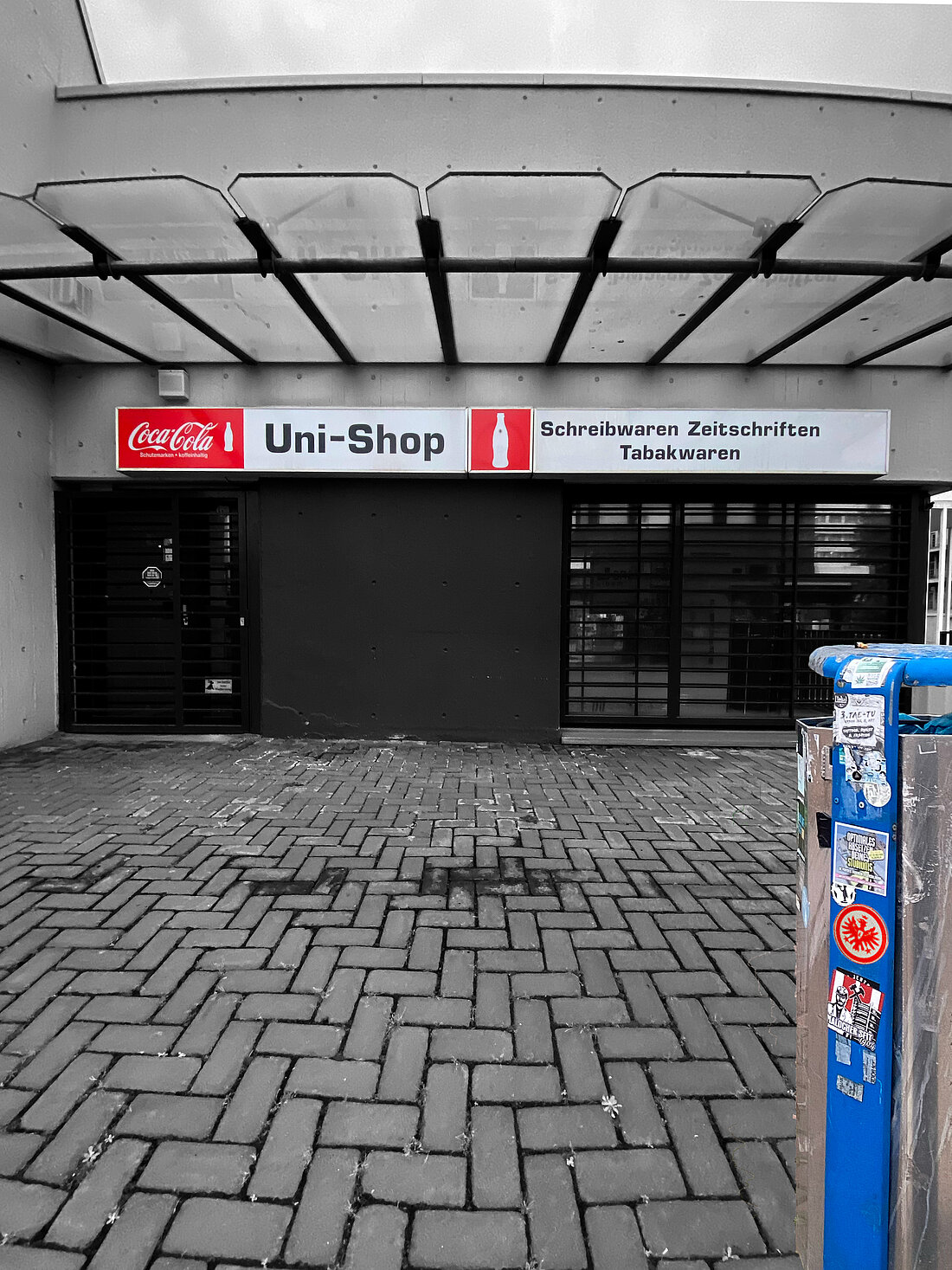 Der Uni Shop auf dem HHU Campus und ein blauer Mülleimer mit vielen Stickern.
