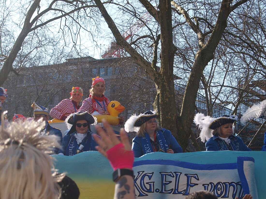 Eine Frau mit einem Entenschwimmring um ihren Bauch auf einem blauen Festwagen mit anderen Frauen.