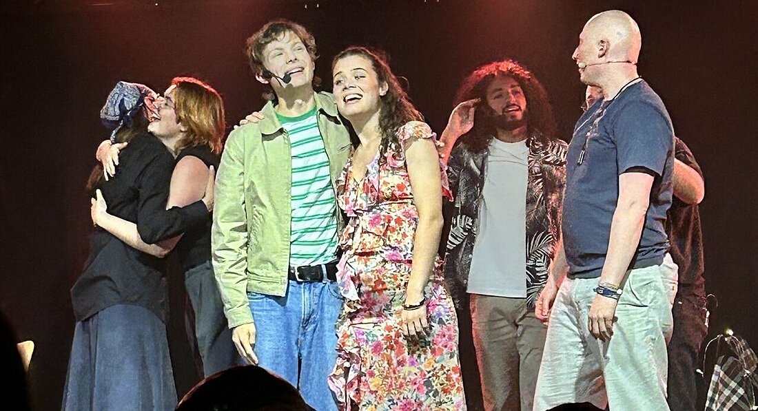 Man sieht das Ensemble des Mensa-Musicals, wie sie sich auf der Bühne liebevoll umarmen.