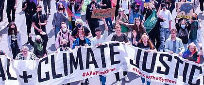 Auf dem Foto ist eine Demonstration von Fridays for Future zu erkennen. Im Vordergrund halten junge Menschen ein Banner auf dem steht „Climate Justice“. Dahinter sind noch viele weitere Menschen mit weiteren Bannern und Plakaten.