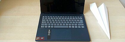 Das Bild zeigt einen Laptop neben dem ein Papierflieger steht