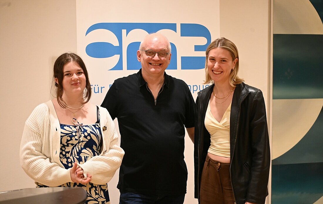 Auf dem Foto sieht man Marie Förder, Andreas Meske und Theresa Schültken, die im Heine-Saal vor einem cm3-Banner stehen