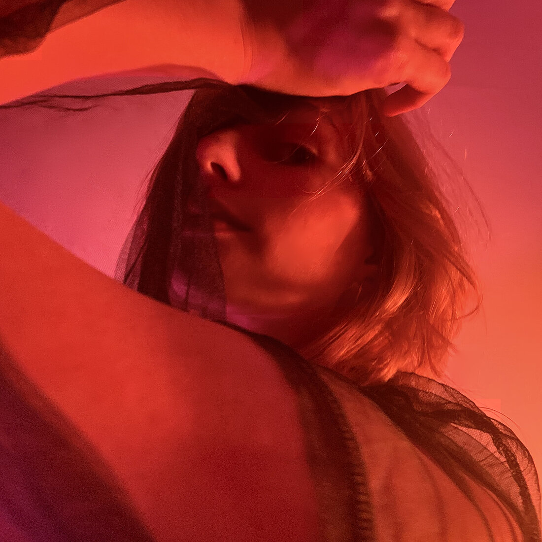 Kira Hummen fährt sich mit einer Hand durch ihr Haar und blickt nach unten in die Kamera. Die Farben sind Pink und Orange durch die gewählte Beleuchtung.