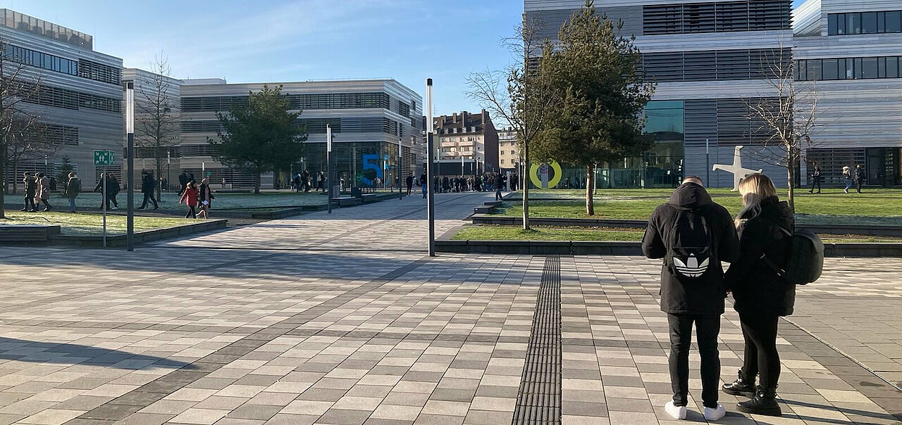 Zu sehen ist der Campus der HSD. Studierende bewegen sich auf dem Campus. 