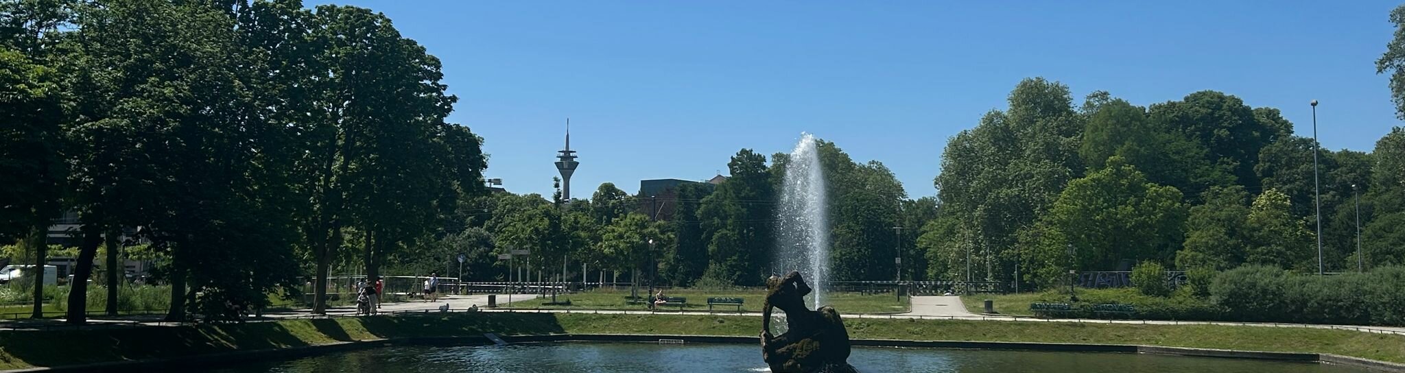 Park mit Fontäne auf einem Gewässer, im Hintergrund der Fernsehturm