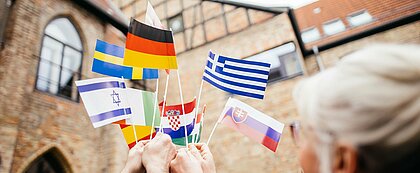 Auf dem Bild sieht man verschiedene Flaagen von Europäischen Ländern, die in die Mitte gehalten werden