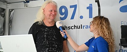 Auf den Foto sieht man Thomas Molck, der in dem mobilen Studio von hochschulradio düsseldorf steht und interviewt wird von hochschulradio düsseldorf