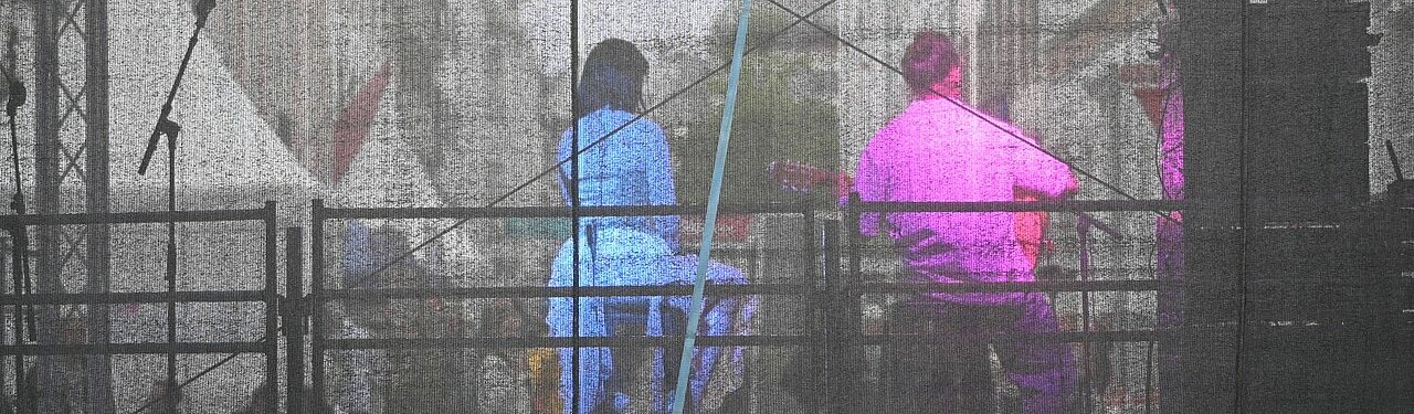 Auf dem Foto sind zwei Musiker von hinten zu sehen. Sie sitzen auf der Bühne und sind in den Farben des Art:Walk Festivals (rosa und blau) beleuchtet.