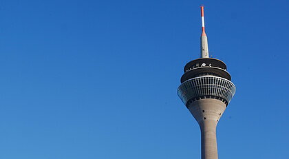 Auf dem Foto sieht man den Rheinturm in Düsseldorf vor dem blauen Himmel