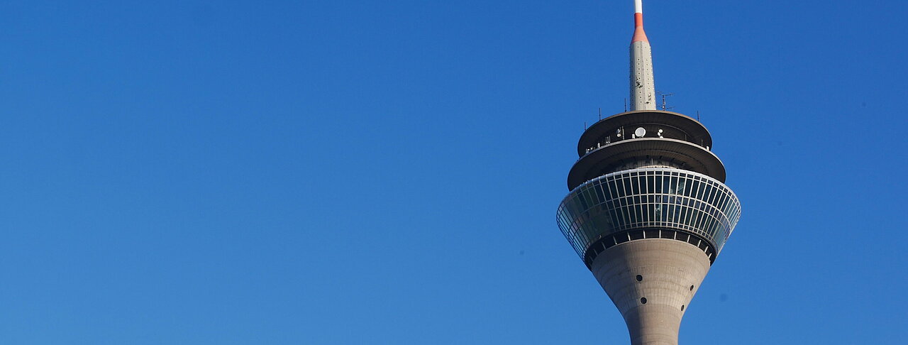Auf dem Foto sieht man den Rheinturm in Düsseldorf vor dem blauen Himmel