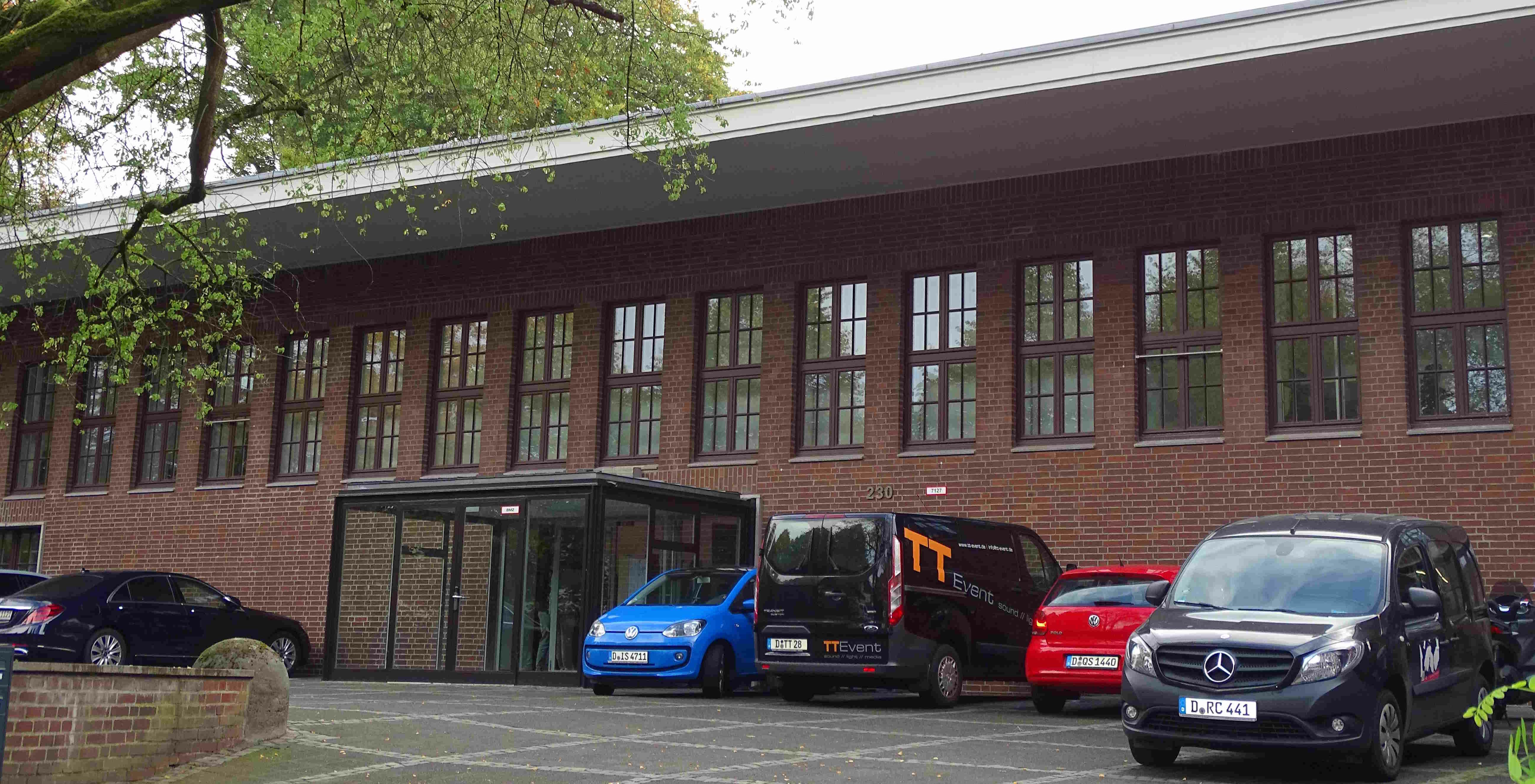 Auf dem Foto it das ZDM zu sehen. Es ist ein längliches Backsteingebäude vor dem Autos stehen. 