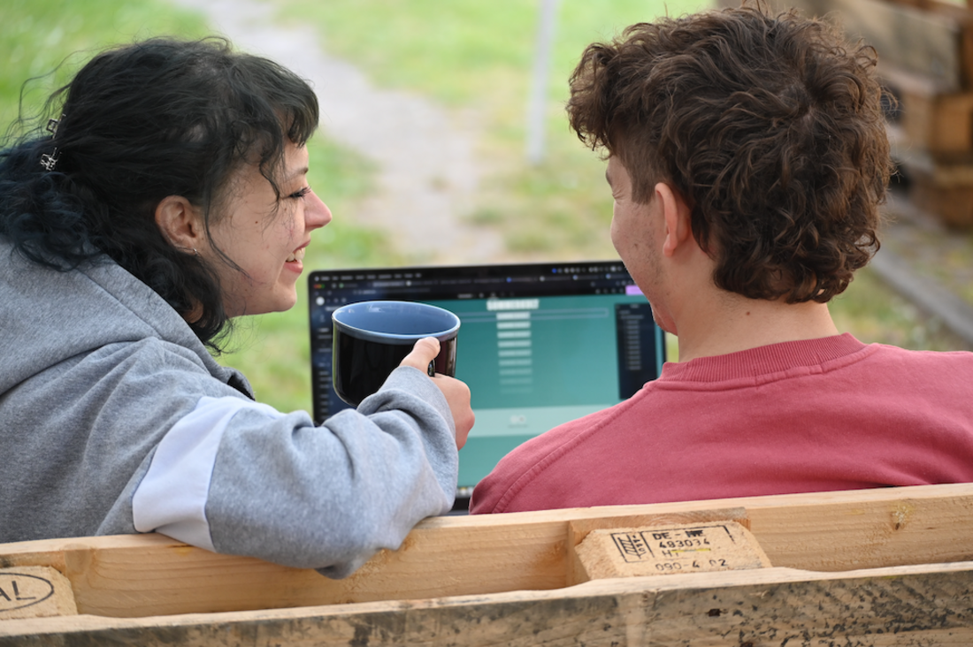 Auf dem Foto sieht man Torben und Emilie von hinten und einen Ausschnitt von dem Laptop auf dem sie die Website planen.