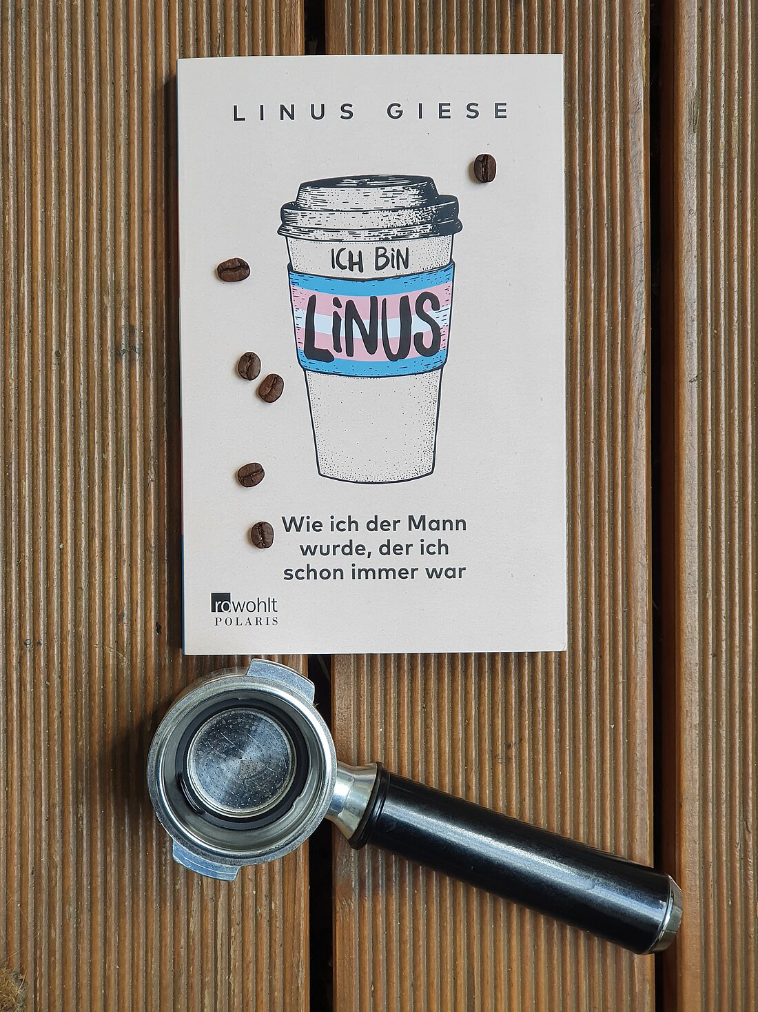 Das Buch "Ich bin Linus" liegt auf Holzdielen mit einem Siebträger und ein paar Kaffeebohnen.
