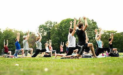 Man sieht eine Gruppe von Menschen, die Yoga machen.