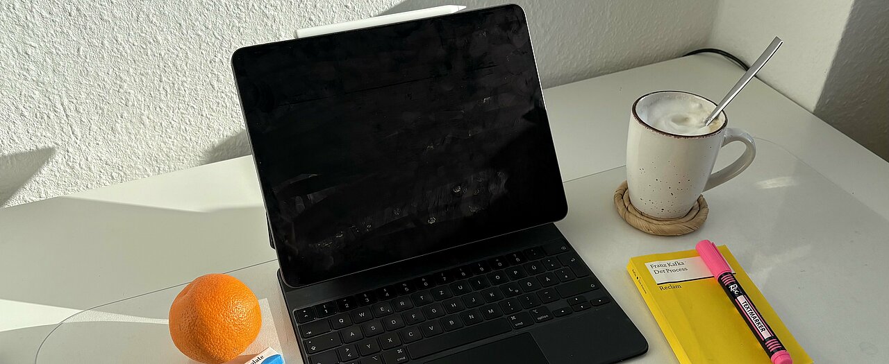 Man sieht eine ruhige Lernumgebung mit iPad, einer Lektüre, einer Tasse Kaffee und Snacks