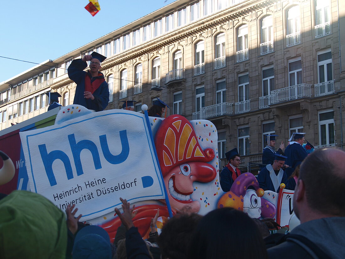 Der Mottowagen der HHU auf welchem auch das Logo der Uni zusehen ist und von welchem ein Professor Süßigkeiten runter wirft.