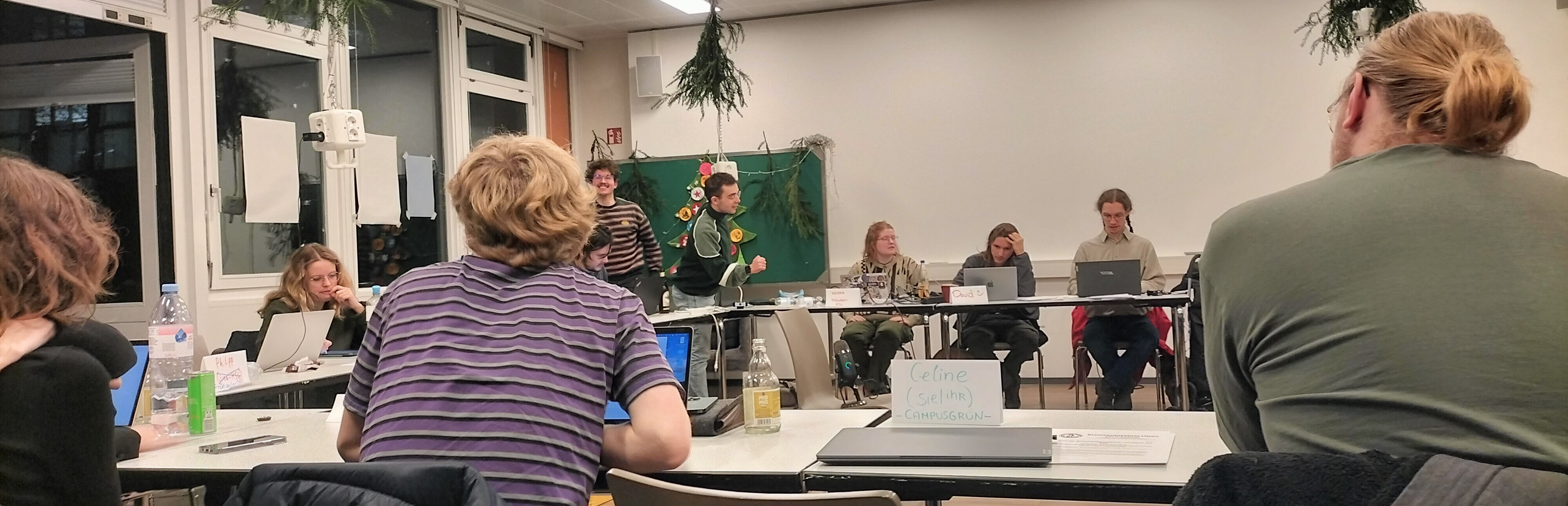 Auf dem Foto sind die Mitglieder des Studierendenparalements zu sehen. Sie sitzen im Kreis an Tischen. 