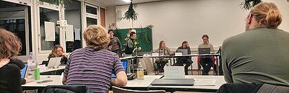 Auf dem Foto sind die Mitglieder des Studierendenparalements zu sehen. Sie sitzen im Kreis an Tischen. 