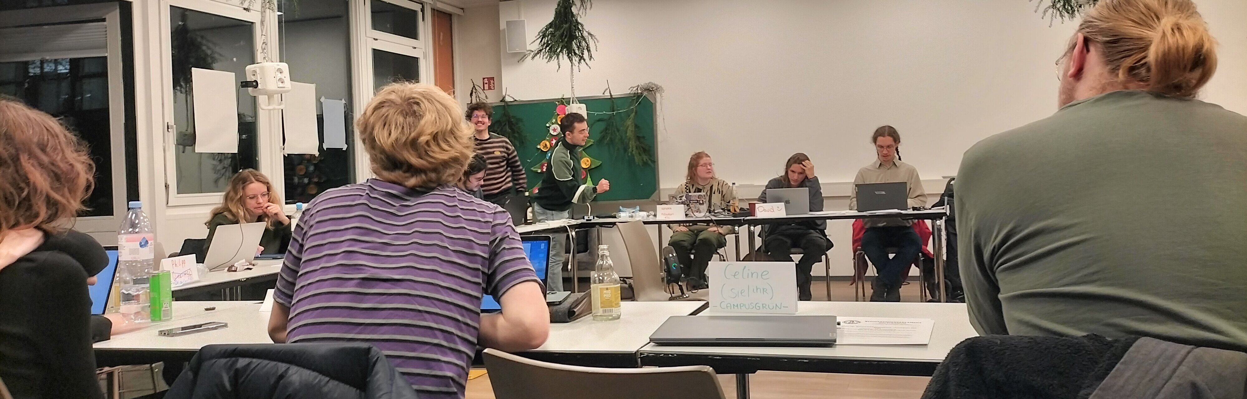 Auf dem Foto sind die Mitglieder des Studierendenparlaments zu sehen. Sie sitzen an langen, weißen Tischen in einem Kreis.