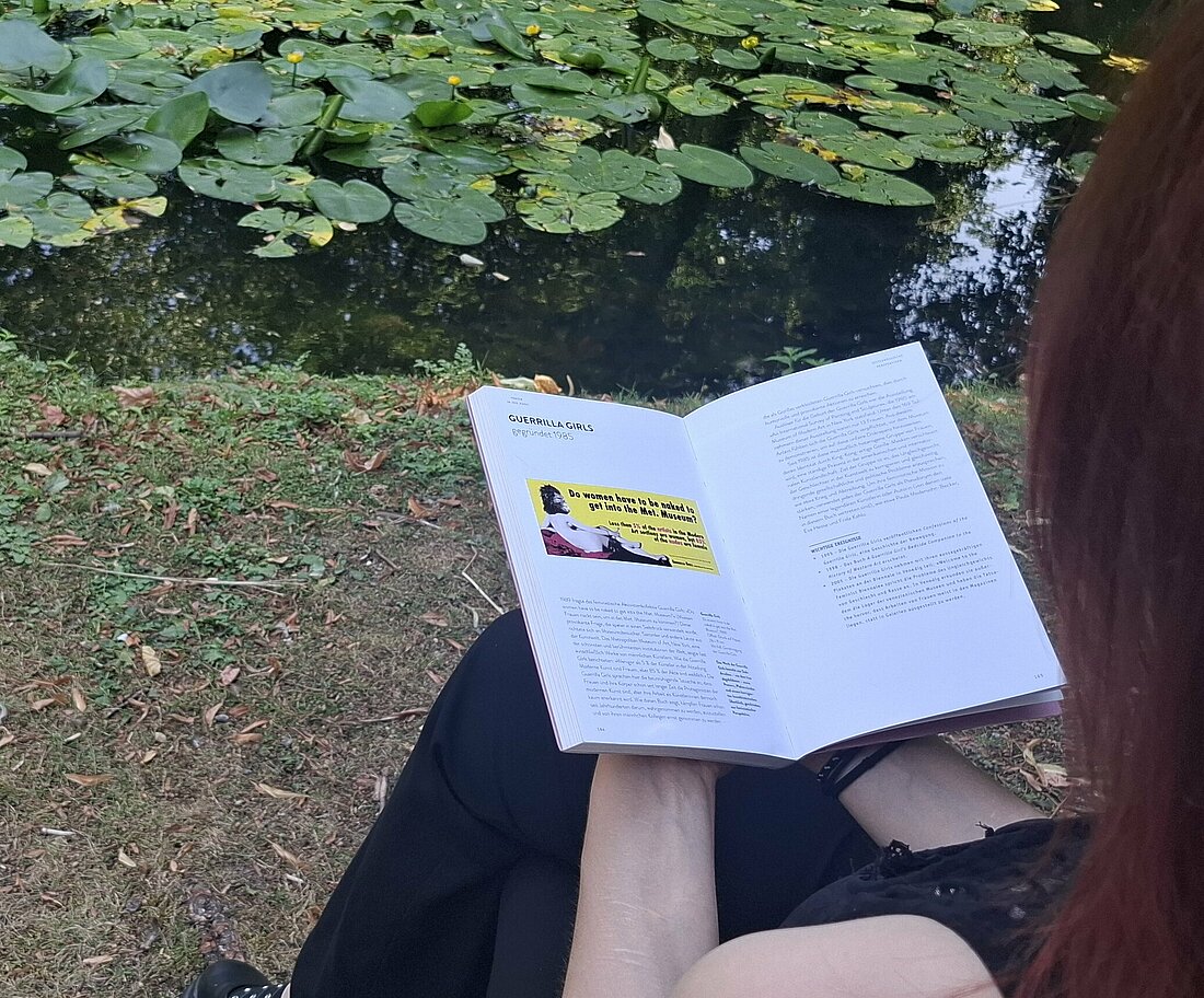 Auf dem Bild sieht man, wie eine Frau ein Buch liest auf dem man das Poster der Guerilla Girls sehen kann.