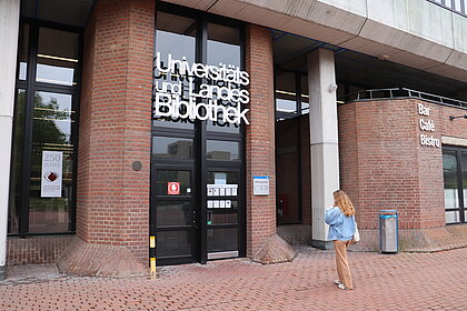 Zu sehen ist ein Mädchen vor dem Eingang der Universitäts- und Landesbibliothek auf dem Campus der HHU.