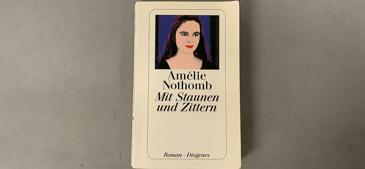 Das Cover der deutschen Version. (Foto: Maximilian Kisters) Das Cover der deutschen Version von "Mit Staunen und Zittern" Darauf, der Titel und der Name der Autorin, Amelie Nothomb und ein Bild ein Frau vor einem dunkelblauen Hintergrund.
