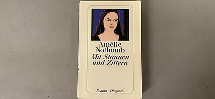 Das Cover der deutschen Version. (Foto: Maximilian Kisters) Das Cover der deutschen Version von "Mit Staunen und Zittern" Darauf, der Titel und der Name der Autorin, Amelie Nothomb und ein Bild ein Frau vor einem dunkelblauen Hintergrund.