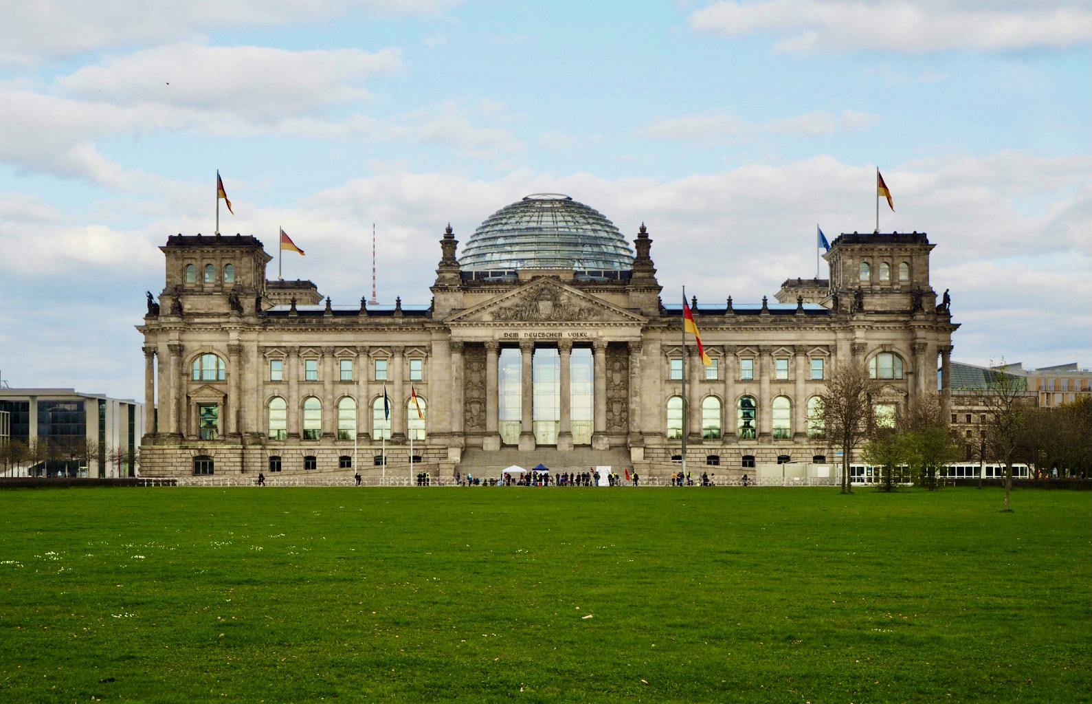 Zu sehen ist das Reichstagsgebäude in Berlin aus frontaler Sicht bei blau-bewölktem Himmel.