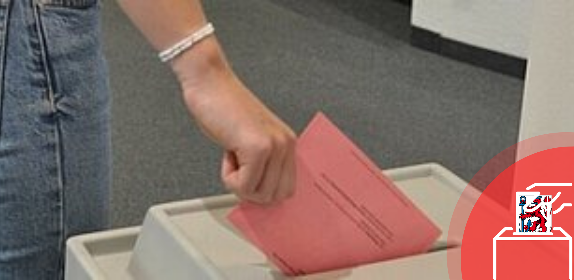Auf dem Foto ist eine Hand zu sehen, die einene roten Wahlzettel in eine Urne wirft.