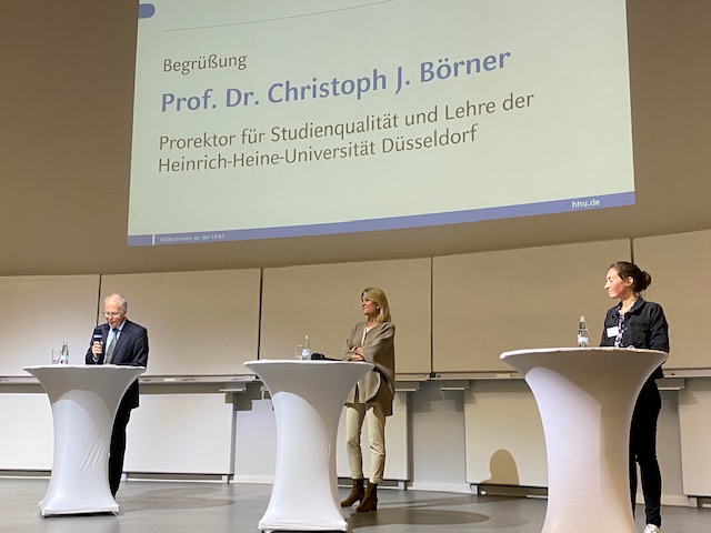 Man sieht die Rektorin Prof. Dr. Anja Steinbeck, Prorektor Prof. Dr. Christoph J. Börner und die Moderatorin Judith Deußen auf der Bühne.